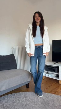 Hanorac alb cu fermoar, top scurt albastru deschis, blugi albastri cu talie înaltă și adidași cu model. Design simplu, materiale moi și croială lejeră.