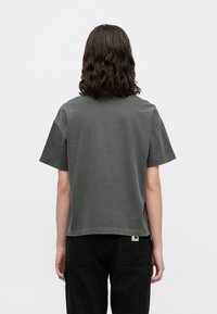 Tumši pelēks kokvilnas T-kreklis ar īsām piedurknēm, brīvs griezums un noapaļota kakla izgriezums. Šūtais etiķete ir redzama apakšējā malu.