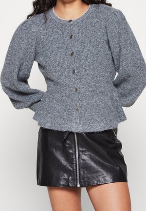 Suéter gris de punto con mangas largas abullonadas, cuello redondo y botones plateados. Combinado con una mini falda de cuero negra con cremallera frontal.