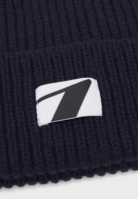 Bonnet en tricot marine avec une texture côtelée et une étiquette blanche avec un motif en zigzag noir cousu sur le devant.