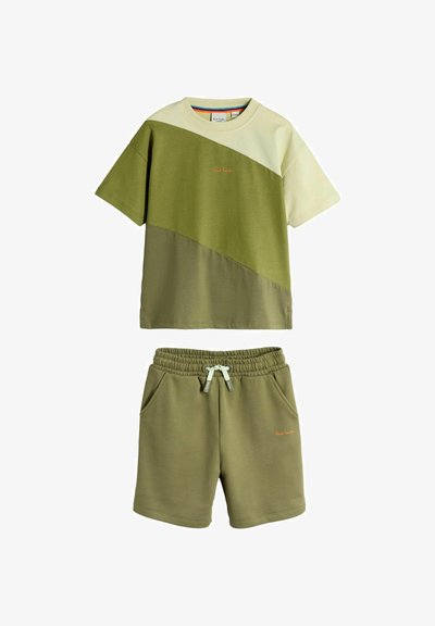 Kortærmet T-shirt med diagonale farveblokke i lys grøn og olivengrøn, kombineret med olivengrønne shorts med snøre i taljen og sidelommer.