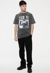 Gray short-sleeved t-shirt featuring a black and white graphic print on the front. Paired with black pants and black boots.