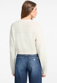 Pull court crème avec un ourlet et des poignets côtelés, associé à un jean en denim bleu taille haute. Les jeans présentent un logo triangulaire sur la poche arrière.