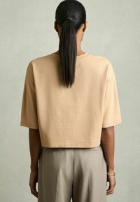 Beige lyhythihaisella cropped t-paidalla, valmistettu pehmeästä puuvillakankaasta. Yhdistetty vaaleanharmaisiin housuihin, joissa on sileä rakenne.