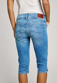 Ljusblå denim capri-jeans med medelhög midja, två bakfickor och en brun läderlapp på midjebandet. Har en lätt blekt finish.