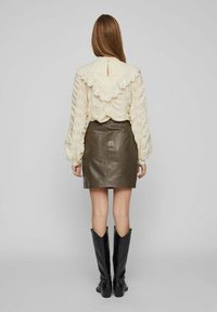 Blouse crème à texture avec un col volé, assortie à une mini-jupe en cuir vert foncé. Des bottes de cowboy noires jusqu'aux genoux complètent l'ensemble.