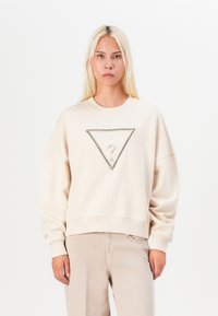 Felpa beige con logo triangolare "GUESS" decorato con strass, spalle scese e polsini a costine in fondo.