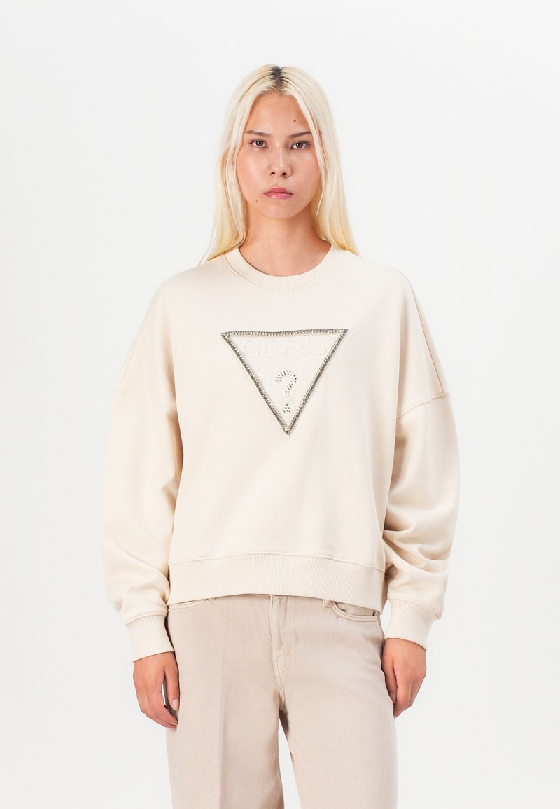 Beige mikina s trojúhelníkovým logem "GUESS" ozdobeným rhinestones, zúženými rameny a žebrovanými lemy na švech.