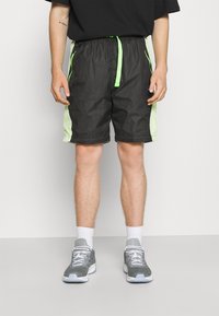 Svarta shorts med neongröna detaljer, elastisk midja och meshsidopaneler. Stylade med grå sneakers och vita ankelstrumpor.