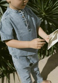 Outfit in denim composto da una camicia a maniche corte con allacciatura a bottoni e pantaloni slim-fit coordinati. Il colore è azzurro chiaro, il tessuto è morbido.