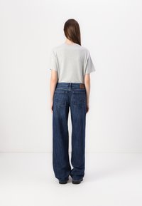 Grey short-sleeve t-shirt with relaxed fit paired with wide-leg dark blue denim jeans featuring back pockets and a leather label on the waistband.