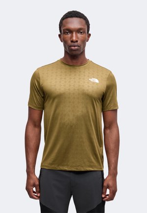 Homme debout, face à l’avant, portant une chemise manches courtes vert olive avec le logo The North Face et un pantalon noir sur un fond uni.
