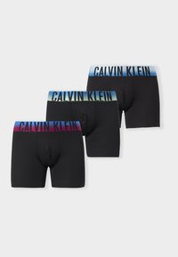 Τρία μαύρα ανδρικά εσώρουχα Calvin Klein με πολύχρωμους διαβαθμισμένους ιμάντες στη μέση σε μπλε, πράσινους και κόκκινους τόνους και το όνομα της μάρκας με μαύρα γράμματα.