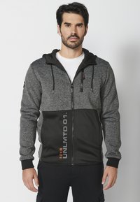 Sudadera con cremallera en gris y negro, con una parte superior texturizada, sección inferior lisa, bolsillos frontales, capucha con cordón y detalle impreso "UNLMTD 01".