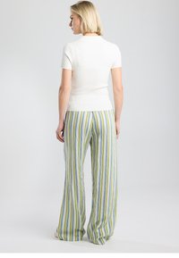 White ribbed short-sleeve top paired with loose, striped pants in green, blue, and yellow. Smooth texture, casual fit, and wide leg design.