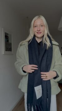 Σκουρόχρωμο μπλε κασκόλ με διακοσμητικές φουντίτσες στις άκρες, κατασκευασμένο από μαλακό υλικό. Φοριέται με παλτό ελιάς από αφράτο ύφασμα. Διαθέτει ετικέτα με την επωνυμία "Barbour".