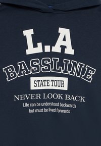 Felpa blu navy con testo bianco: "L.A BASSLINE," "STATE TOUR," "NEVER LOOK BACK," e "La vita può essere compresa all'indietro, ma deve essere vissuta in avanti."