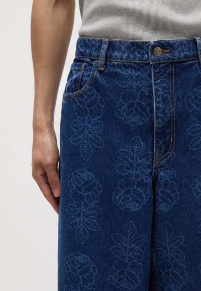 Shorts en denim bleu marine arborant un motif floral discret, cinq poches et des coutures contrastées au niveau de la taille et des coutures.