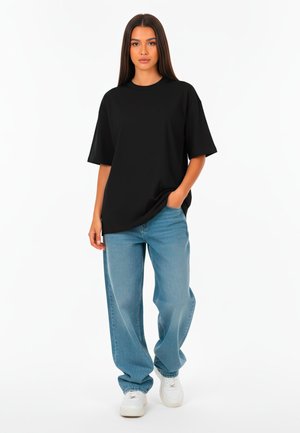Black oversized t-shirt with short sleeves, paired with light blue loose-fitting jeans and white sneakers. Plain design, no patterns or accents.
