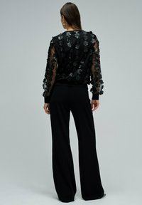 Blouse noire ornée de fleurs avec des manches transparentes, associée à un pantalon noir à jambes larges. Encolure ronde simple et poignets ajustés.