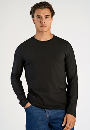 Zwarte lange mouwen T-shirt van zachte stof, met een ronde halslijn en een aansluitend ontwerp, gecombineerd met blauwe denim jeans.