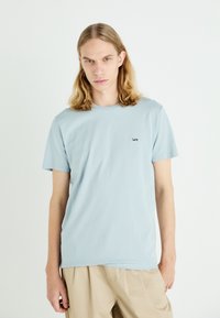 Camiseta de algodón azul claro con cuello redondo y mangas cortas. Presenta un pequeño logotipo negro de "Lee" en el pecho. Textura suave, corte relajado.