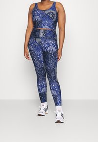 Navy patterned sports bra and leggings set featuring paisley and geometric designs. Model wears white sneakers with black accents.