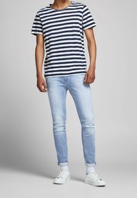 Marinblå och vitrandig t-shirt med kort ärm, kombinerad med ljusblå skinny jeans och vita sneakers. Mjuk bomullsmaterial, avslappnad passform.