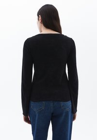 Schwarzes Langarmoberteil mit glatter Textur und Rundhalsausschnitt, kombiniert mit blauen, hochgeschnittenen Jeans, die über Gesäßtaschen und eine leichte Ausbleichung verfügen.