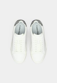 Λευκά δερμάτινα αθλητικά παπούτσια με λεία επιφάνεια, διακοσμημένα με γκρι καπάκι στη φτέρνα, κορδόνια και μινιμαλιστικό σχέδιο. Το λογότυπο είναι ορατό στη σόλα.