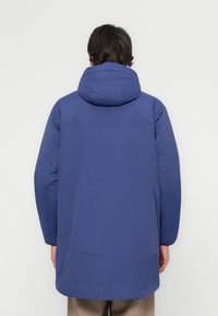 Blå hettejakke med lange ermer, glatt tekstur og en enkel, rett snitt. Har en baksømm og minimale design detaljer.