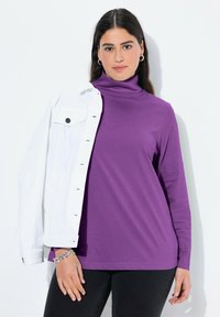 Lila langärmliger Rollkragenpullover aus glattem Stoff, kombiniert mit einer weißen Jeansjacke; zeichnet sich durch eine lockere Passform und charakteristische Nähte aus.