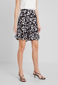 Černá sukně s bílým květinovým vzorem, vrstvené volány na lemu, lehký materiál, délka po kolena, doplněná černými páskovými podpatky.