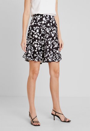 Czarna spódnica z białym wzorem kwiatowym, warstwowe falbany na dole, lekki materiał, do kolan, w zestawie z czarnymi sandałami na obcasie.