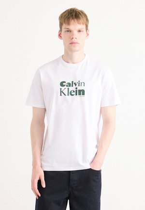 White cotton t-shirt featuring a green "Calvin Klein" logo in a modern font. Short sleeves and a classic crew neck design.