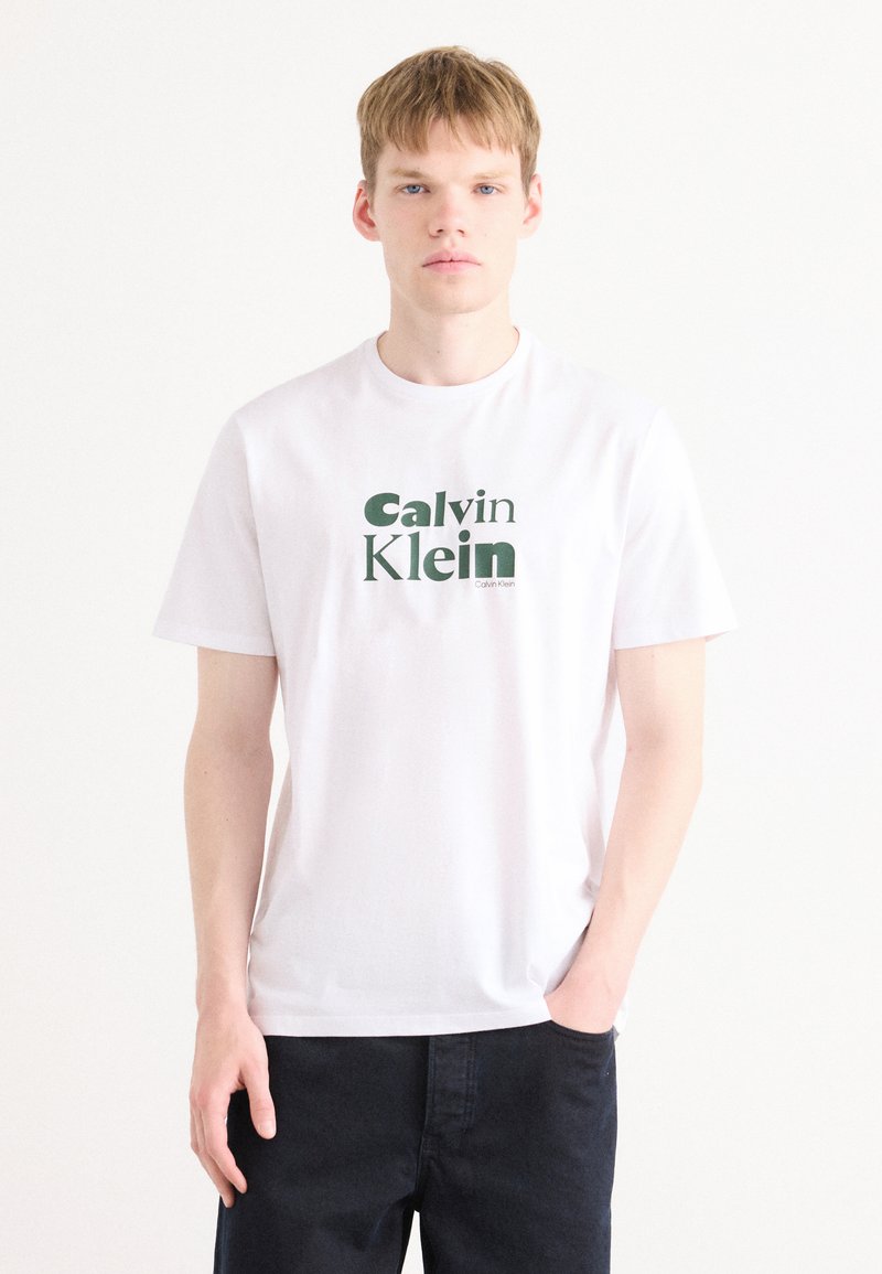 Hvit bomull t-skjorte med en grønn "Calvin Klein" logo i en moderne skrifttype. Korte ermer og klassisk rund halsdesign.
