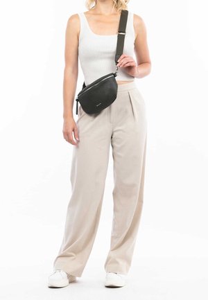 Nainen pukeutuneena valkoiseen ribbineulottuun lyhyeen toppiin, beigen värisiin leveälahkeisiin housuihin, valkoisiin lenkkareihin ja mustaan säädettävällä hihnalla varustettuun olkalaukkuun.