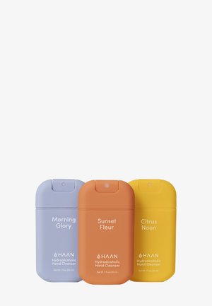 Trzy butelki środka do mycia rąk: lawendowa, pomarańczowa i żółta plastikowa, z zaokrąglonymi nakrętkami; oznaczone etykietami "Poranna Chwała", "Zachodnia Fleur" i "Cytrusowe Południe."