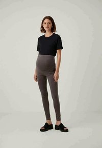 Conjunto de maternidade composto por uma t-shirt preta justa e leggings cinzas de cintura alta, feitas de um tecido suave, combinadas com sandálias de plataforma pretas.