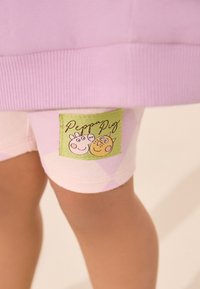 Roza hlačne kratke hlače z argyle vzorcem, z zeleno etiketo s karikaturama dveh likov iz Risanke o Pujsi Pepi. Mehka tkanina, elastičen pas.