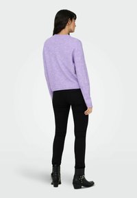 Pull en tricot lilas à manches longues, encolure ronde et ourlet côtelé, accompagné d'un jean skinny noir et de bottines.