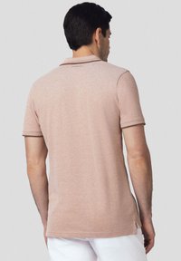 Jasnoróżowa koszulka polo z krótkimi rękawami, teksturowana tkanina, kontrastowe ciemne wykończenia kołnierzyka i rękawów, boczne rozcięcia dla wygody.