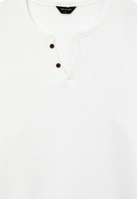 Camicia henley bianca in cotone con un motivo testurizzato, scollatura a V e due bottoni marrone scuro al colletto. Etichetta del marchio: Calliope.