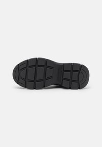 Suela de zapato de goma negra con un patrón de tracción rugoso. Presenta una puntera redondeada y una ranura central para mayor flexibilidad, diseñada para ofrecer tracción y durabilidad.