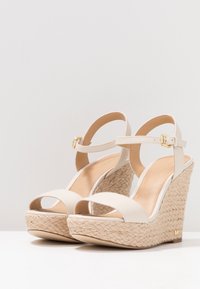 Sandali a zeppa beige con design espadrille, dotati di una suola in corda testurizzata e di un delicato cinturino alla caviglia con dettaglio in fibbia dorata.