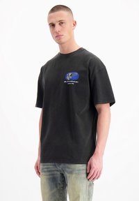 Zwarte katoenen T-shirt met een relaxte pasvorm, ronde hals en korte mouwen. Aan de voorkant staat een blauw en wit grafisch logo. De tekst luidt "Official Fuel."