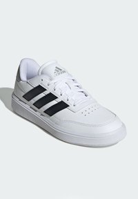 White athletic shoe with black three stripes, smooth leather upper, padded collar, and flat rubber sole. Features perforations for breathability.
