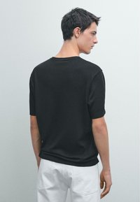 Černé tričko s krátkým rukávem a kulatým výstřihem, vyrobené z hladkého materiálu. Záda mají čistý, minimalistický design a jemnou texturu.