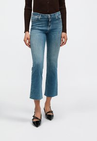 Φαρδιά τζιν από ανοιχτό γαλάζιο ντένιμ με άψητο τελείωμα και διακριτική ξεθώριαση, συνδυασμένα με μαύρες γόβες από δερμάτινο βινύλιο με μυτερή μύτη.