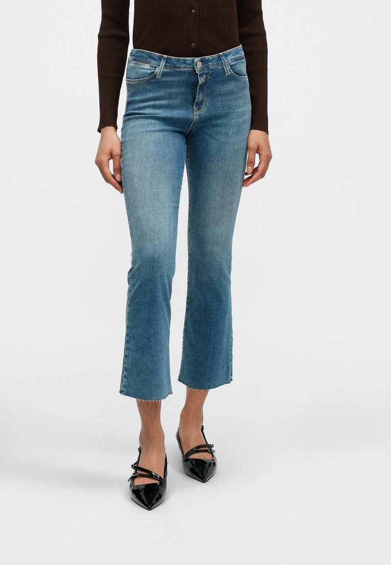 Φαρδιά τζιν από ανοιχτό γαλάζιο ντένιμ με άψητο τελείωμα και διακριτική ξεθώριαση, συνδυασμένα με μαύρες γόβες από δερμάτινο βινύλιο με μυτερή μύτη.